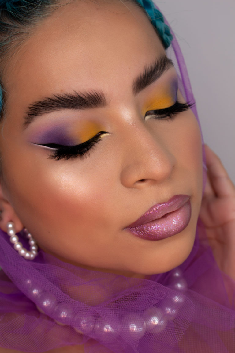 Ana Paola Mendoza Makeup con un maquillaje en tonos morados y amarillos en los ojos, los labios degradados en diferentes tonos lilas y las cejas al estilo lion mane